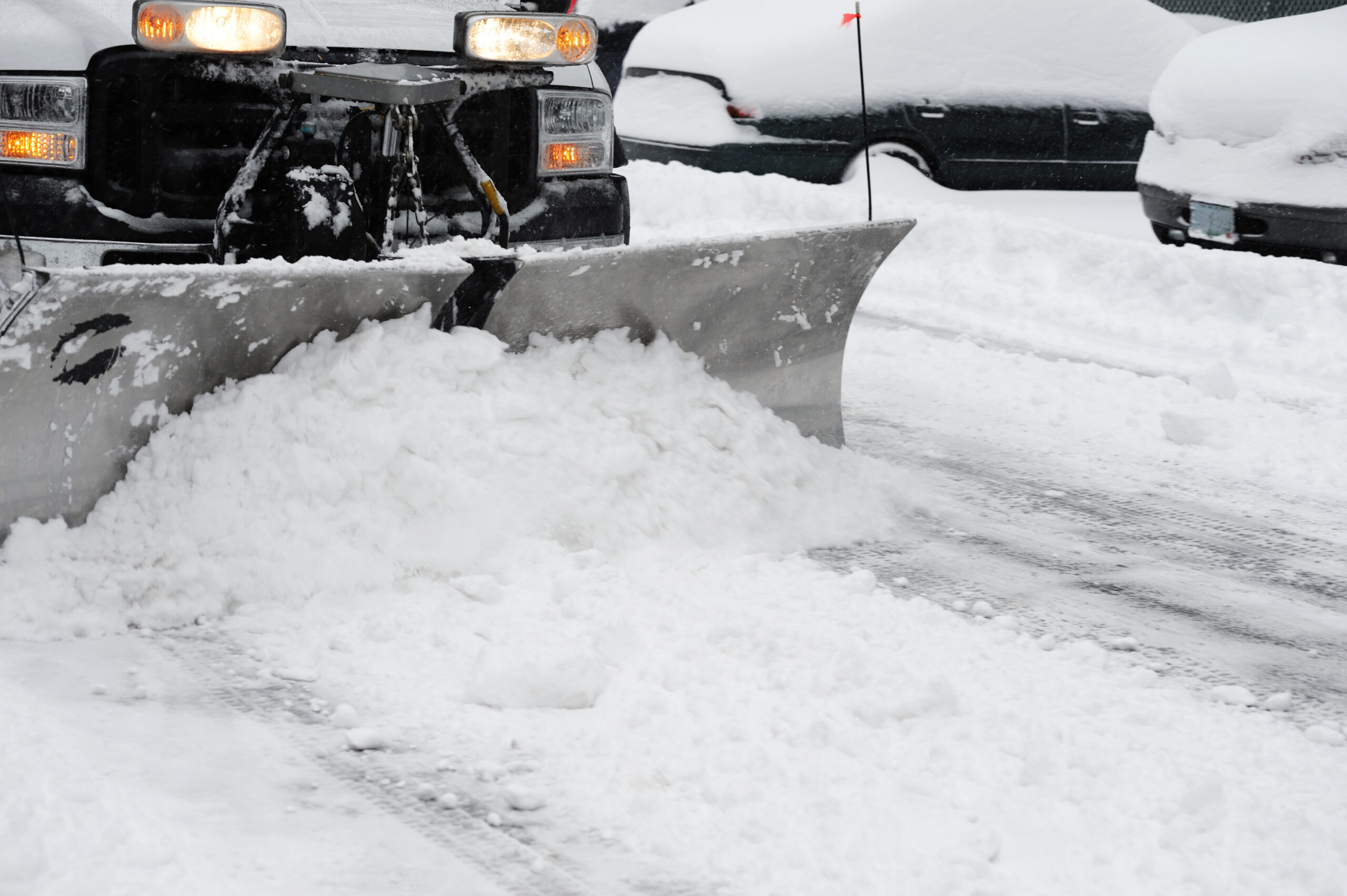 Powerhouse snow plow clearing commercial parking lot during winter storm.